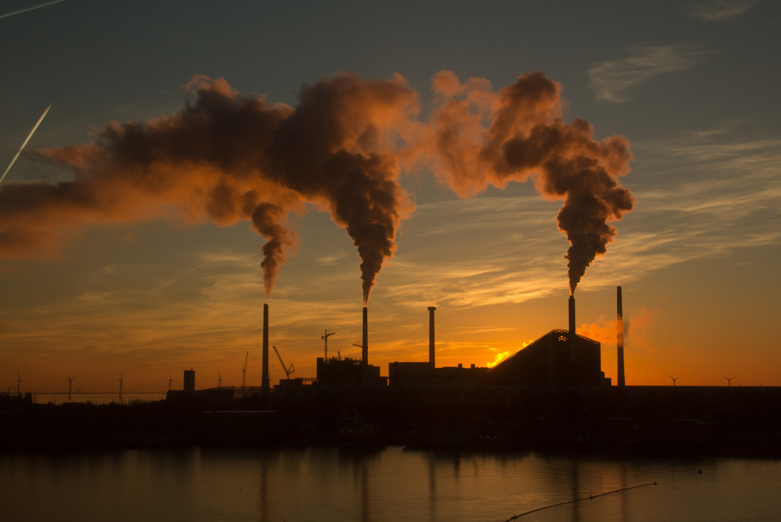  A low angle shot of a factory with smoke and steam coming out of the chimneys captured at sunset